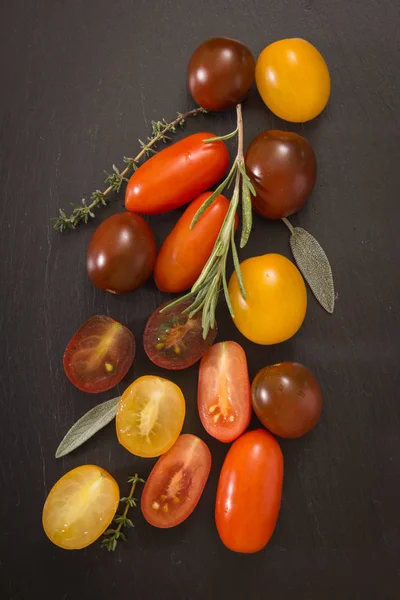 Colorful cherry tomatoes cluster with herbs, on black background.