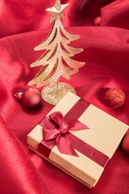 Noel süsler ile dalgalı kırmızı saten kumaş üzerine fiyonklu hediye kutusu.