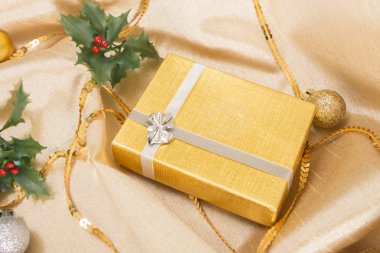 Noel süsler ile altın dalgalı saten kumaş üzerine fiyonklu hediye kutusu.
