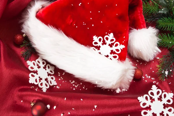 Капелюх Санти з різдвяними прикрасами та снігом, на червоній хвилястій тканині . — стокове фото