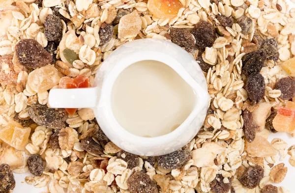 White milk pot with plant milk, on pile of muesli with dry fruits, closeup background.