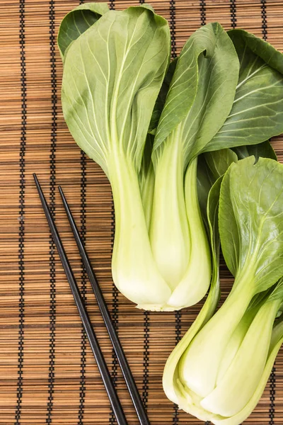 Bunch of fresh green baby bok choy with chopsticks , on bamboo placemat background — Stock Photo, Image