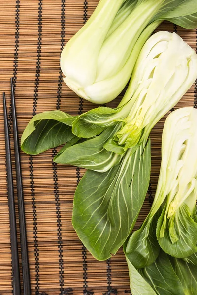 Bunch of fresh green baby bok choy with chopsticks , on bamboo placemat background — Stock Photo, Image