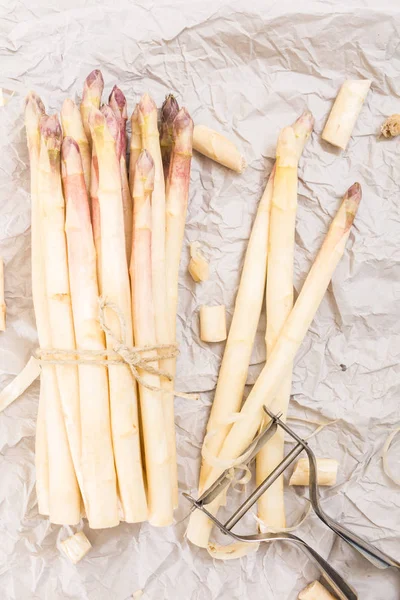 Bunch of white asparagus with peelings, on crumpled paper and metallic peeler. — Stock Photo, Image
