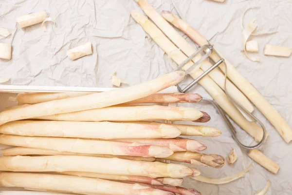 Bunch of white asparagus in box, on crumpled paper with metallic peeler. — Stock Photo, Image