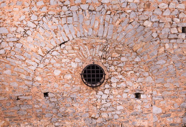 Mur en pierre avec fenêtre ronde et barreaux métalliques, d'une ancienne forteresse . — Photo