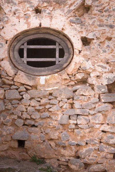Kamenná zeď s kulatým dřevěným oknem středověké pevnosti. — Stock fotografie