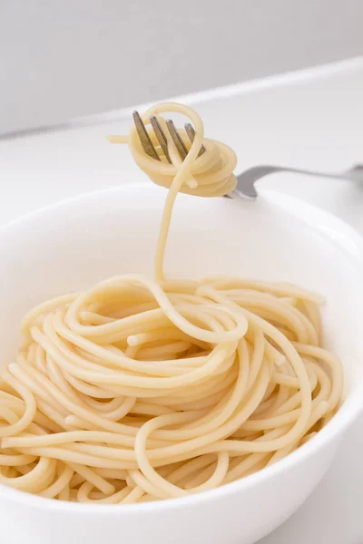 Gewone gekookte spaghetti pasta in witte kom en op de voorvork, op witte achtergrond. — Stockfoto