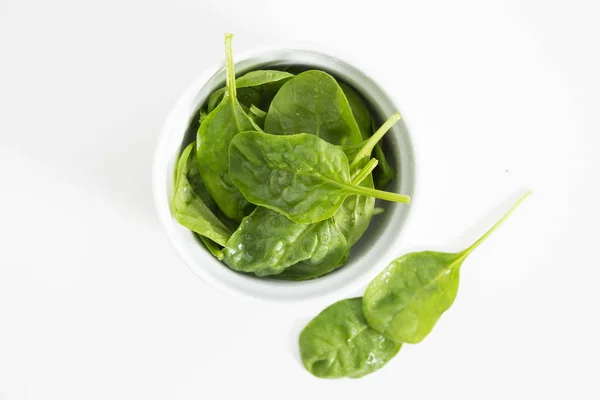 Frische nasse grüne Babyspinatblätter in einer Schüssel, Nahaufnahme auf weißem Hintergrund. — Stockfoto