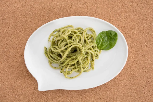 Pasta de espaguetis con salsa de pesto en plato blanco en forma de burbuja de chat, sobre fondo de corcho . —  Fotos de Stock