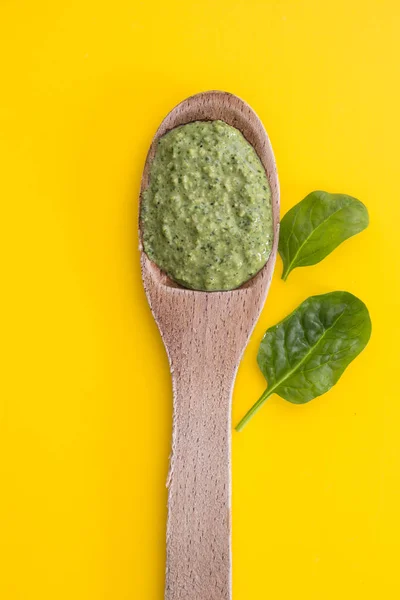 Molho de pesto verde acabado de fazer na colher de madeira, close-up no fundo amarelo . — Fotografia de Stock