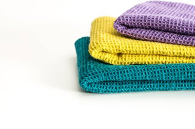 Beyaz zemin üzerine düzgünce katlanmış renkli mutfak havlu yığını.