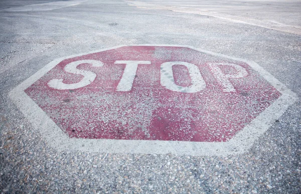 Weathered red hexagon stop sign painted on roads pavement surface, closeup background.