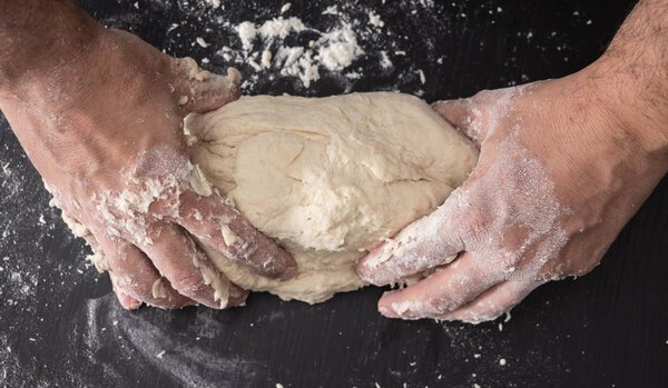 Male hands kneading dough, baking preparation closeup.