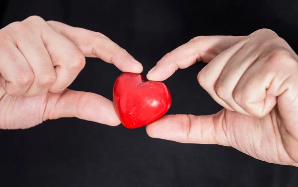 Αρσενικό χέρια που κρατούν closeup κόκκινη καρδιά, σε μαύρο φόντο. — Φωτογραφία Αρχείου