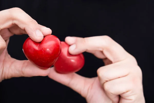 Manos masculinas sosteniendo dos corazones rojos, primer plano sobre fondo negro . — Foto de Stock