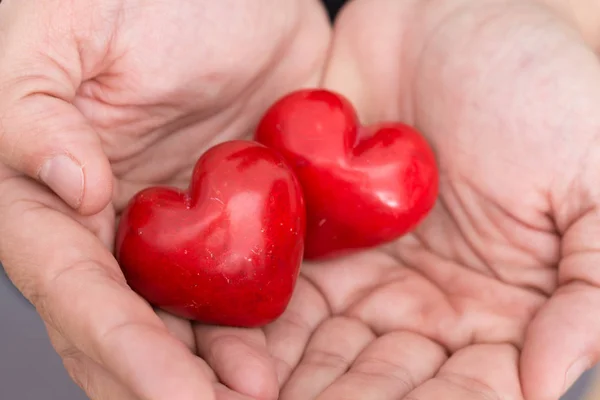 Mãos masculinas segurando dois corações vermelhos, fundo close-up . — Fotografia de Stock