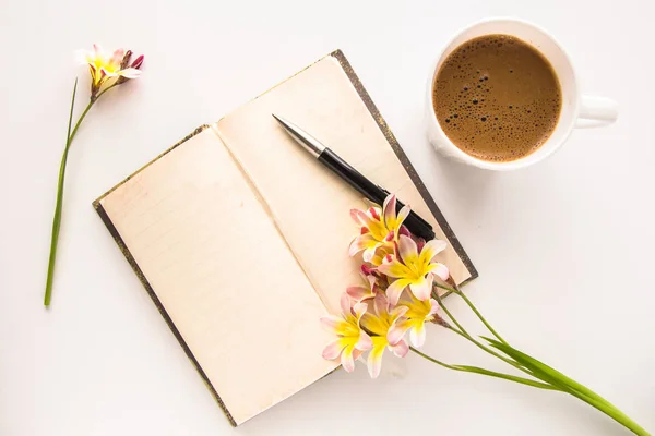 Kleurrijke Lentebloemen, met lege open dagboek voor tekst en kopje koffie op witte achtergrond. — Stockfoto