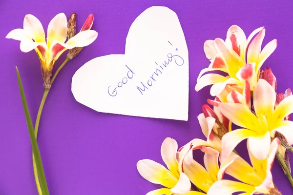 Note in shape of heart with words "Good Morning!" with flowers on purple surface. — Stock Photo, Image