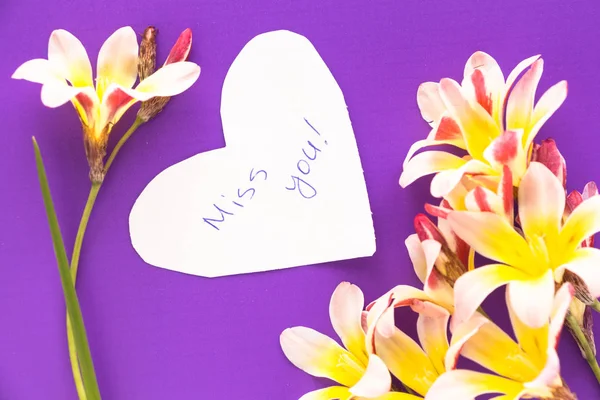 Note en forme de cœur avec des mots "Miss You !" avec des fleurs sur la surface violette . — Photo