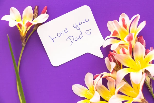 Note in shape of heart with words "Love you Dad!" with flowers on purple surface. — Stock Photo, Image