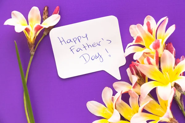 Nota en forma de corazón con palabras "¡Feliz Día del Padre!" con flores en la superficie púrpura . —  Fotos de Stock