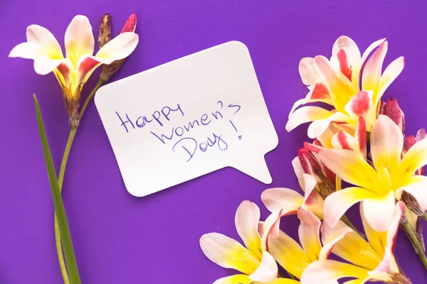 Notă în formă de inimă cu cuvintele "Happy Women 's Day!" cu flori pe suprafata violet . — Fotografie, imagine de stoc