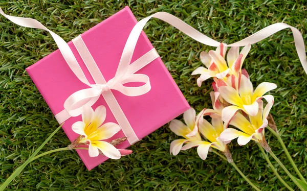 Caja de regalo rosa con lazo y flores, sobre hierba verde . — Foto de Stock