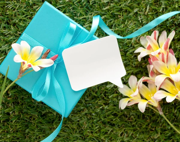 Niebieskie pudełko z kokardą, puste Uwaga do tekstu i kwiaty na zielonej trawie. — Zdjęcie stockowe