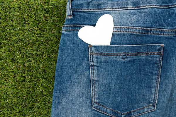 Blank note in shape of heart with copy-spce in blue jeans back,pocket, on green grass. — Stock Photo, Image