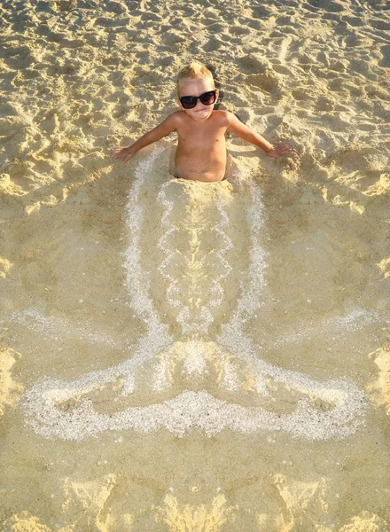 El niño en gafas del sol en la orilla del mar jugando con la arena —  Fotos de Stock