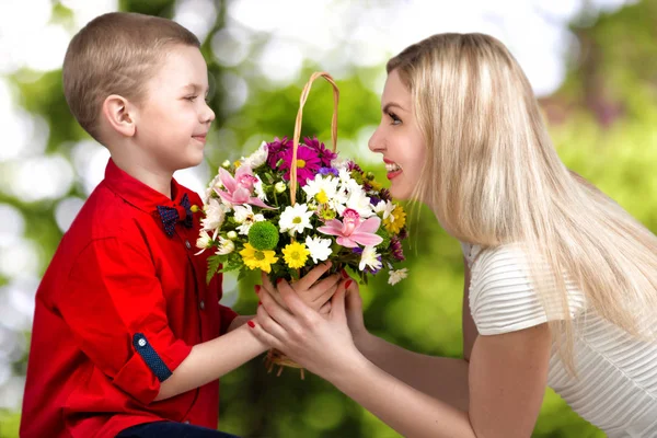 Unga vackra mamma med sin son. En kvinna och en pojke med en bukett, en korg med blommor. Våren begreppet familjesemester. Kvinnodagen. — Stockfoto