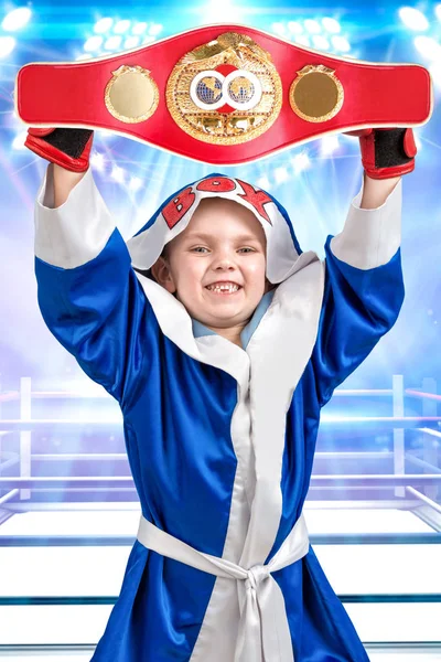 Boxer de menino pequeno segurando o cinturão de campeão de boxe. O atleta de bata no fundo do anel. Pequeno campeão. — Fotografia de Stock