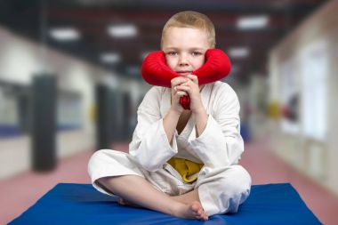Eldiven ile spor salonunda oturan çocuk atlet karate. Karate salonunda mindere.