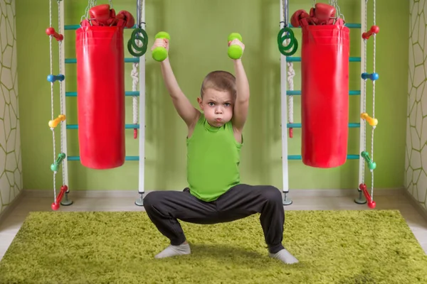 Een kleine jongen voert een oefening met halters. Het kind hurkt met halters. Sport, gezonde leefstijl. — Stockfoto
