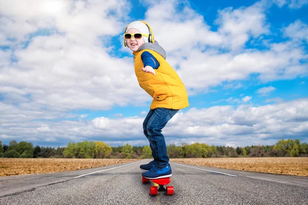 Chico haciendo trucos en un monopatín, patinar en la carretera.El niño en el estilo de Hip Hop. El Joven Rapero. . — Foto de Stock