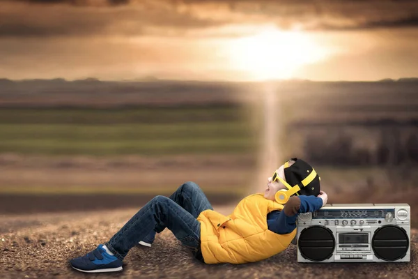 Estilo chico hip-hop, escuchando grabadora vintage, acostado en un camino de campo . — Foto de Stock