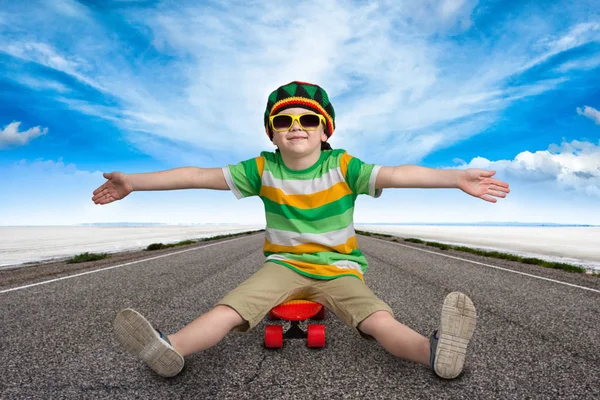 Menino sentado em um skate na estrada.Esportes extremos.Moda infantil . — Fotografia de Stock