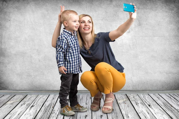 Ung mamma och Lille son är fotograferade på en mobiltelefon som gör selfie. Snygga, trendiga, moderna — Stockfoto