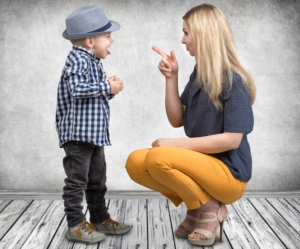 En ung mamma skäller sin stygga lilla son. Pojke visar tungan och retar min mamma. — Stockfoto