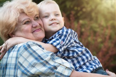 Küçük çocuk şefkatle sevgili büyükannesi kucaklar. Nesiller seviyorum.