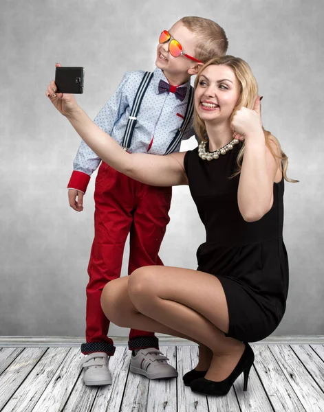 Młoda matka i syn są fotografowane na telefon komórkowy, co selfie. Stylowe, modny, nowoczesny — Zdjęcie stockowe