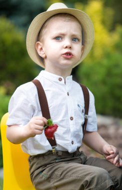 Küçük çocuk olgun güzel kokulu çilek yeme hasır şapkalı.
