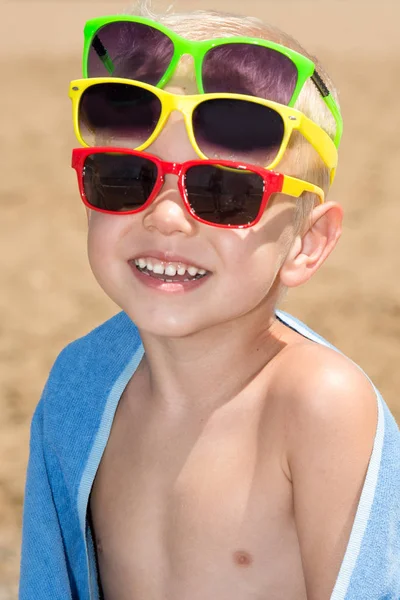 Un niño pequeño en gafas de sol brillantes, tomando el sol en la playa — Foto de Stock
