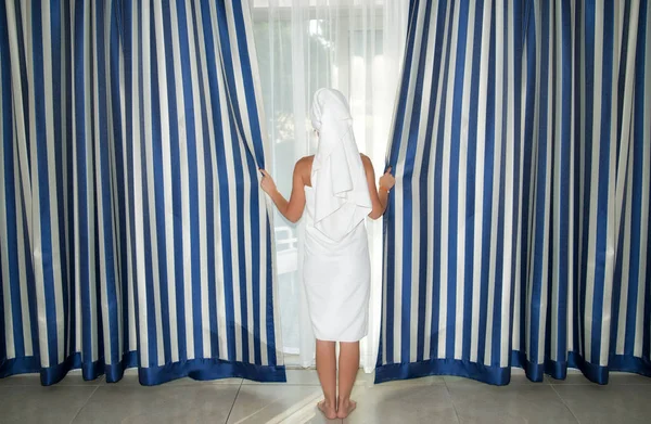 Νεαρή γυναίκα στην πετσέτα μπάνιου ανοίγει τις κουρτίνες στο δωμάτιο. — Φωτογραφία Αρχείου
