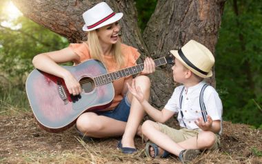 Genç anne ve güzel bir oğlan dinlenme ormandaki şarkı şarkıları bir gitar altında.