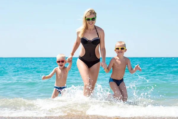 Mooie moeder en twee mooie zoon bedrijf handen uitgevoerd op de golven. Leuk, gezinsvriendelijke zomervakantie. — Stockfoto