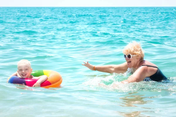 Grandmother and little grandson swim in the sea.The baby in the bouncy multicolored circle.Summer vacation.