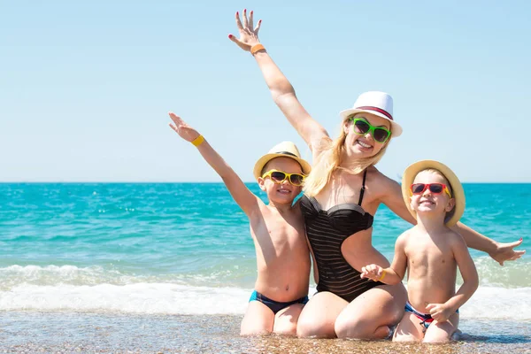 Moeder en twee zonen in hoeden zittend op het strand. Zomer familie vakantie. — Stockfoto