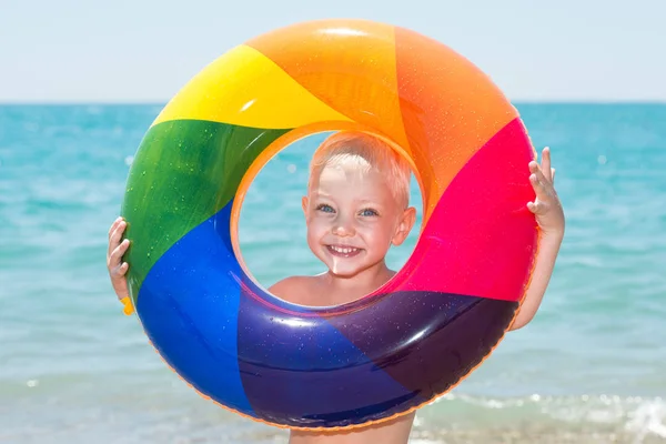 Niño feliz jugando con el anillo inflable colorido en día caliente del verano. Juguetes de agua infantil. Los niños juegan en el resort tropical. Vacaciones familiares en playa — Foto de Stock
